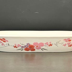 Puede incluir: Fuente de cerámica blanquecina con diseño floral. La fuente ovalada presenta un delicado patrón de flores rosas, rojas y moradas con tallos verdes. Adecuada para servir alimentos.
