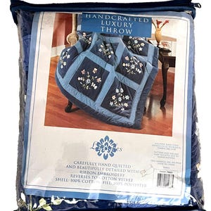 May include: A packaged handcrafted luxury throw. The throw is navy blue with embroidered floral details. The packaging reads "Handcrafted Luxury Throw" and "Carefully hand quilted and beautifully detailed with ribbon embroidery."