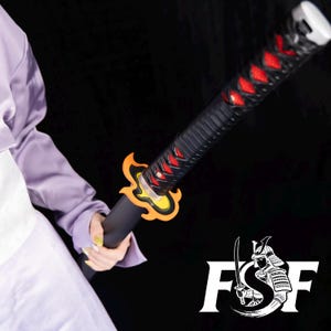 Pode incluir: Uma espada katana preta com uma empunhadura vermelha e preta e uma guarda amarela e laranja. A espada é segurada por uma pessoa vestindo uma camisa roxa. O logotipo de um samurai está no canto inferior direito.