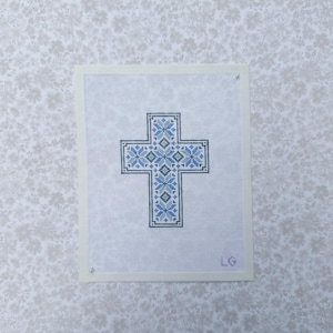 May include: A rectangular piece of white needlepoint canvas featuring a cross design stitched in shades of blue, grey, and black. The cross is composed of intricate geometric floral patterns. The initials LG are stitched in the bottom right corner.