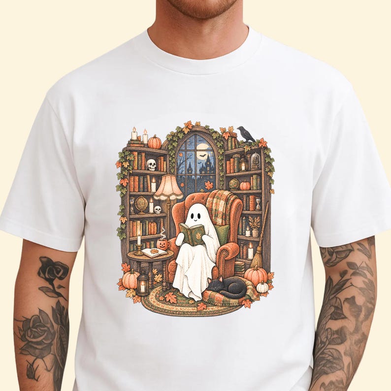 May include: A white t-shirt featuring a graphic illustration of a ghost sitting in an orange armchair, reading a book. The scene includes bookshelves, a lamp, a black cat, pumpkins, and autumn leaves, set against a window with a night view.