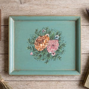 May include: A rectangular, turquoise serving tray with a hand-painted floral design. The flowers are in shades of peach and pink, surrounded by green leaves. The tray has a distressed, vintage look.