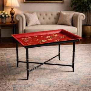 May include: A red rectangular serving tray with a floral design sits on a black table with bamboo-style legs. The tray's surface has a detailed painting of flowers and birds. The table is a decorative accent piece, ideal for a living room.