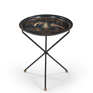 Puede incluir: Una bandeja ovalada negra con un diseño decorativo de pájaros y flores, sostenida por un soporte de metal negro. El borde de la bandeja es dorado y el soporte tiene un diseño de tres patas con pies dorados.
