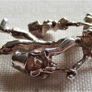 May include: A silver charm depicting two figures holding buckets, possibly representing a pair of chimney sweeps.