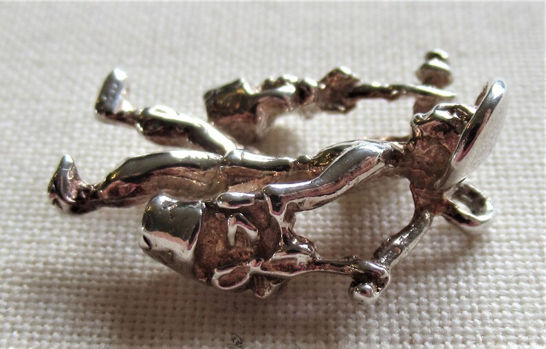 May include: A silver charm depicting two figures holding buckets, possibly representing a pair of chimney sweeps.