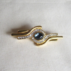 May include: Gold tone brooch with a blue cabochon stone surrounded by clear rhinestones. The brooch is shaped like a wave.