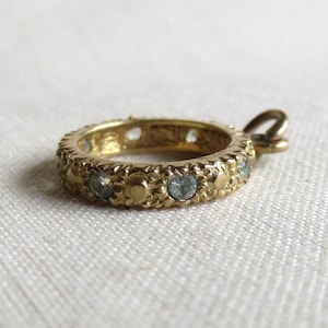 May include: A gold-toned metal ring pendant featuring a textured surface with alternating small circular studs and embedded clear, round-cut stones. The circular band includes a small attached jump ring loop at the top for hanging purposes.