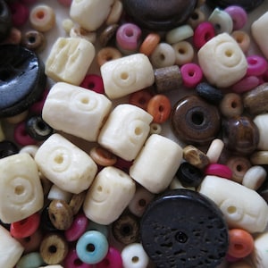 May include: A selection of beads in various shapes, sizes, and colours. The beads include off-white, cylindrical beads with a circular design, along with dark brown, pink, and orange beads. Suitable for jewellery making and crafts.