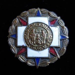 May include: A gold-coloured pin with a white cross and a blue and red star design. The pin features the text "National Auxiliary" and a small image of people in uniform.
