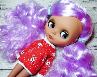 May include: A doll with long, curly, lavender hair wearing a red and white floral sweater. The doll has large, blue eyes and a light pink complexion.