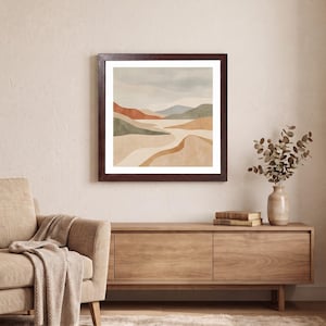 Könnte beinhalten: Ein quadratischer Kunstdruck in einem Rahmen, der eine abstrakte Landschaft mit geschichteten Hügeln in gedeckten Tönen von Beige, Hellbraun, Terrakotta, Salbeigrün und sanftem Blau zeigt, eingefasst in einen dunkelbraunen Holzrahmen.
