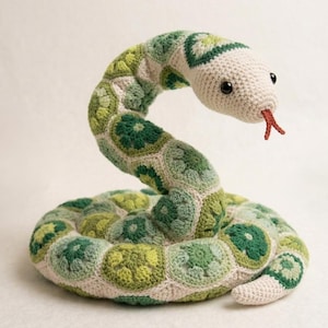 Peut inclure: Un serpent en peluche enroulé, fabriqué à partir de nombreux hexagones crochetés dans diverses nuances de vert, allant du vert citron au vert forêt foncé. La tête est blanc cassé avec des yeux en plastique noir et une langue rouge crochetée.