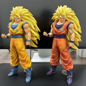 Puede incluir: Dos figuras de acción de un personaje con pelo amarillo puntiagudo, vistiendo trajes naranjas y azules. Las figuras tienen cuerpos musculosos y posan en una postura dinámica. Cada figura tiene un cinturón azul y botas azules.