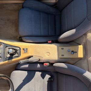 Könnte beinhalten: Innenraum eines Autos mit dunkelblauen Stoffsitzen, einer beigefarbenen Mittelkonsole und einem schwarzen Lenkrad. Das Bild zeigt den Schalthebel, die Handbremse und die Sicherheitsgurtschnallen.