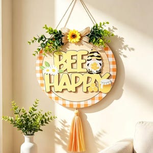 Könnte beinhalten: Ein rundes Holzschild für die Wand mit einem gelb-weißen Karomuster am Rand und dem Schriftzug BEE HAPPY in erhabenen gelben Buchstaben. Das Schild ist mit einem Zwerg, einem Honigtopf, weißen Gänseblümchen, einer Sonnenblume und einer Quaste verziert.