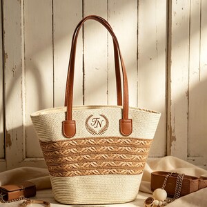 May include: A cream and brown woven straw tote bag with brown leather handles. The bag has a decorative woven pattern. The initials "TN" are embroidered within a wreath on the front of the bag.