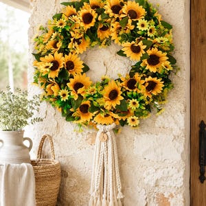 May include: A vibrant sunflower wreath with a macrame accent, perfect for seasonal decor. The wreath features bright yellow sunflowers with dark brown centers and green leaves. A wooden tag with the letter "A" hangs from the macrame.