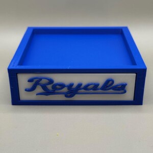 May include: A blue and white box with the word "Royals" in script. The box has a blue interior and a white panel with the word "Royals" in blue script. The box is likely a decorative item or storage container.