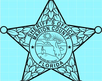 May include: Black and white Sheriff's Office badge from Marion County, Florida, in a star shape. The badge has a circular center with a landscape scene and the text "IN GOD WE TRUST". The text "SHERIFF'S OFFICE MARION COUNTY FLORIDA" is also visible.