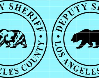 May include: Two circular emblems with a light blue background. Each emblem features a black bear silhouette inside a black ring. The text "DEPUTY SHERIFF LOS ANGELES COUNTY" is written around the bear in black.
