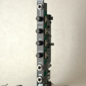 May include: A black electronic module with the text "BD606 CV/GT" and several knobs labelled "Accent", "Tone", "Mix", and "Level". It has input and output jacks and a small logo. Additional electronic components are scattered nearby.
