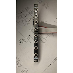 May include: A black electronic module labelled "uMult" with multiple input jacks. The module has a series of silver-coloured jacks and is mounted on a circuit board diagram. A ribbon cable extends from the top. The module is approximately 13 cm long.