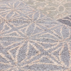 May include: Close-up of a gray rug with a geometric pattern. The rug features a repeating design of interlocking shapes in a lighter beige color against a gray background. The texture appears soft and plush.