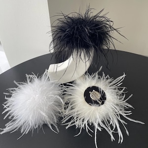 Peut inclure: Ensemble d'accessoires en plumes, comprenant une coiffe en plumes noires et blanches et deux broches en plumes blanches. Les broches ont une attache à épingle. Les accessoires sont sur une surface noire.