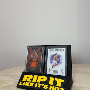 May include: Black display stand with two football trading cards. The cards are in protective cases. The stand has the text "RIP IT LIKE IT'S HOT" in yellow letters.