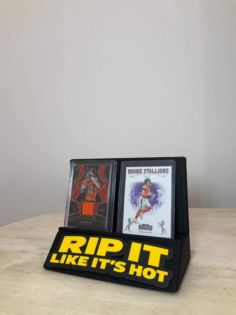 May include: Black display stand with two football trading cards. The cards are in protective cases. The stand has the text "RIP IT LIKE IT'S HOT" in yellow letters.
