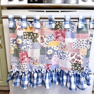 May include: A patchwork oven door cover with a variety of floral and patterned fabric squares. The top has blue and white gingham tabs with buttons. The bottom edge features a blue and white gingham ruffle.