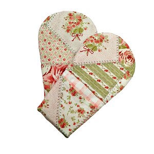 May include: Two quilted oven mitts with a floral pattern. The mitts are made of various fabric patches in shades of red, green, and white. Each mitt features a floral bouquet design with a red bow. The mitts are stitched together with a decorative stitch.