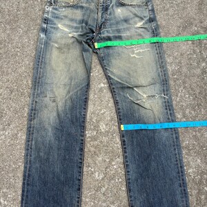 K&ouml;nnte beinhalten: Verblasste blaue Jeans aus Denim mit abgenutzten Details, einschlie&szlig;lich Rissen und Gebrauchsspuren. Die Jeans haben ein klassisches F&uuml;nf-Taschen-Design und einen Knopf- und Rei&szlig;verschluss. Ma&szlig;e in Zentimetern.