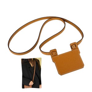 May include: A tan leather crossbody pouch featuring a textured surface, white contrast stitching, and a thin adjustable shoulder strap. The pouch has a rectangular body with two top tabs secured by small gold-toned metal studs and hardware.