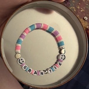 May include: A colorful bracelet with the word "GRANTEE" spelled out in white letter beads. The bracelet features a mix of blue, pink, purple, and white disc-shaped beads. Smiley face beads are on each end.