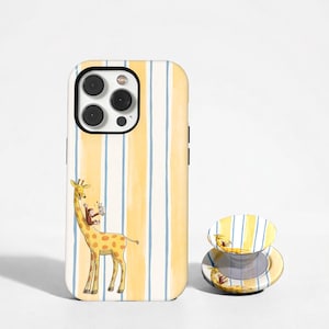 Puede incluir: Una funda de teléfono y un soporte para teléfono con una ilustración de jirafa y mono. La funda tiene un fondo a rayas amarillas y blancas con detalles azules. El soporte para teléfono tiene un diseño a juego.