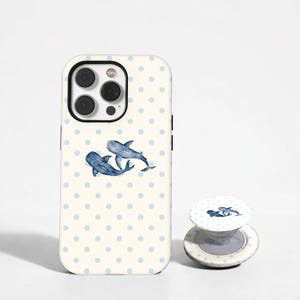 Può includere: Una custodia per smartphone e un supporto circolare per telefono abbinato con sfondo color crema, un motivo a pois azzurri e due balene blu scuro in stile acquerello che nuotano insieme al centro della custodia e del supporto.