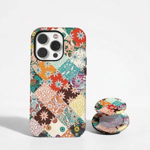 Könnte beinhalten: Eine rechteckige Smartphone-Hülle und ein passender runder, zusammenklappbarer Handyhalter mit einem lebendigen, mehrfarbigen Patchwork-Design. Das Muster besteht aus verschiedenen quadratischen Kacheln, die mit komplexen Blumenmotiven, Paisley-Wirbeln und geometrischen Formen in Rot-, Orange-, Gelb-, Türkis- und Brauntönen verziert sind.