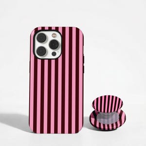 May include: A pink and burgundy striped phone case and matching phone grip. The phone case is designed to fit a smartphone, and the grip is a round, collapsible stand. The background is white.