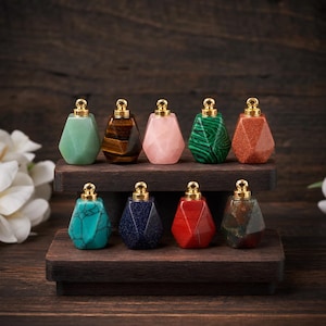 May include: Nine gemstone pendants in assorted colours, such as green, brown, pink, and red, each with a gold-coloured cap. The pendants are displayed on a dark wooden stand against a blurred wooden background.