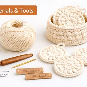 Puede incluir: Un surtido de materiales y herramientas de ganchillo, que incluye una madeja de hilo color crema, un ganchillo de madera, una aguja de metal y varias etiquetas hechas a mano. La imagen también presenta una cesta y posavasos, todos hechos con un diseño de ganchillo color crema. El texto "Materials & Tools" es visible.