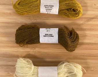 May include: Three skeins of wool yarn in different colors: mustard yellow, dark brown, and cream. The yarn is labeled "Appleton Bros. Ltd. London" and "100% Wool Made in England".