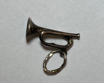 May include: A small, silver-colored bugle charm with a loop for attachment. The bugle has a flared bell and a curved body. The charm is likely made of metal and is designed to be a pendant or a decorative element.