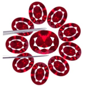 Può includere: Una collezione di nove pietre preziose rosso intenso dal taglio ovale, disposte in un motivo circolare. Ogni pietra presenta una superficie sfaccettata che riflette la luce, creando un motivo a stella bianco brillante al centro. Una pinzetta metallica tiene una pietra.