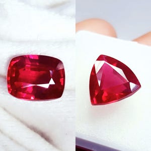 May include: Two faceted red gemstones. On the left, a cushion-cut ruby with a rectangular shape and rounded corners. On the right, a triangular-cut ruby with sharp points. Both stones exhibit deep red hues and clear, reflective surfaces.