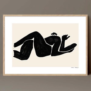 Könnte beinhalten: Abstrakter Kunstdruck einer schwarzen Tintenfigur in einem Naturholzrahmen. Das Kunstwerk zeigt eine liegende Form mit kräftigen Pinselstrichen auf cremefarbenem Hintergrund. Ein minimalistisches Design für moderne Wohnkultur.