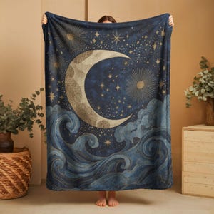 May include: A rectangular throw blanket featuring a dark blue night sky with a large, textured crescent moon, radiating suns, and scattered stars. The lower portion displays stylized, swirling ocean waves in shades of blue and gold.