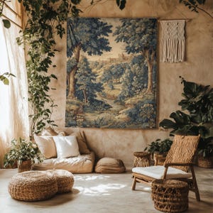 Op de afbeelding: Een groot wandtapijt met een landschap met bomen, een rivier en een stad in de verte. Het wandtapijt is het middelpunt van een kamer met natuurlijk licht, planten en geweven meubels, wat een gezellige, bohemien sfeer creëert.