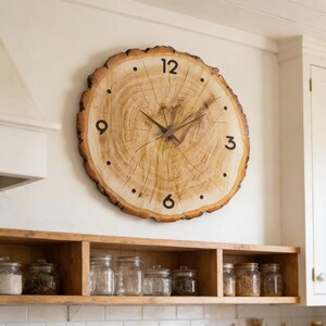 May include: A large, round wall clock made from a cross-section of a tree trunk. The clock face features black numerals at the 12, 3, 6, and 9 o'clock positions, with small dots marking the other hours. The clock hands are dark brown.